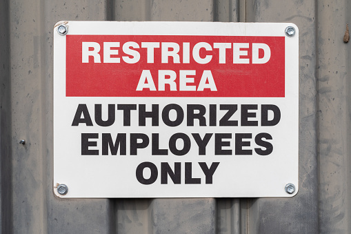 A caution sign reading “restricted area authorized employees only” bolted onto a metal plate wall.