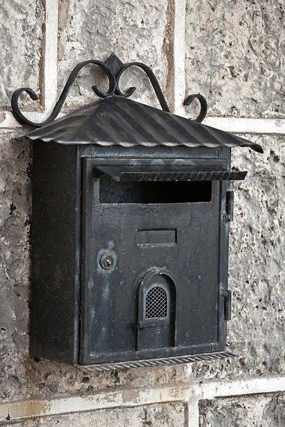 istock Old weathered black metal mailbox mounted on gray stone wall 180233196