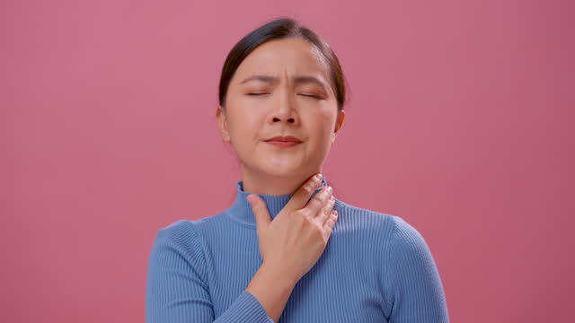 Close-up shot of woman was sick with sore throat, standing isolated on pink background.