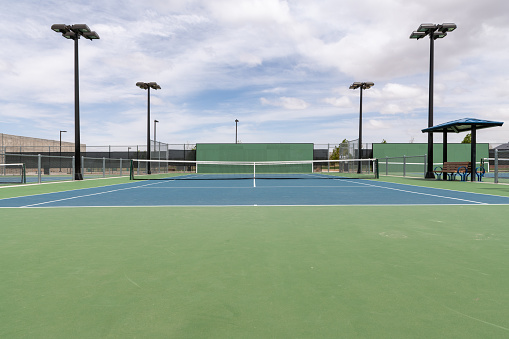An empty public tennis court during the day with a partly cloudy sky.