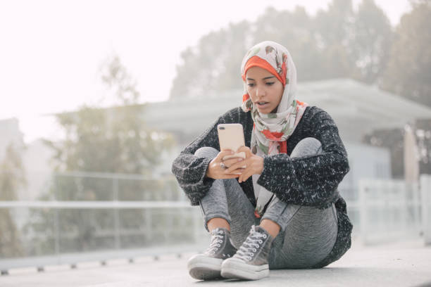 istock Young student sitting on parka bench and texting on mobile 1802367134