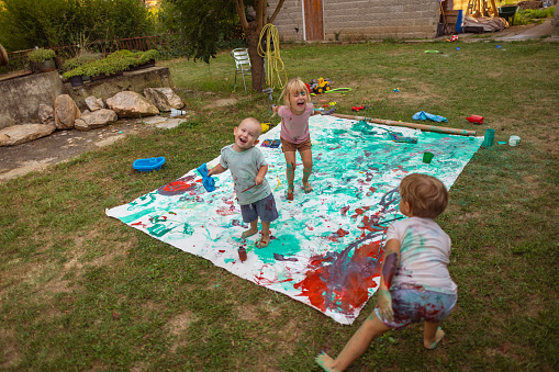 A couple of children enjoying watercolor painting on a big canvas in the backyard