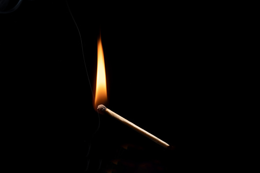 A yellow and orange  flame coming from an ignited wood match. Blue background ... Copy space on the flame.