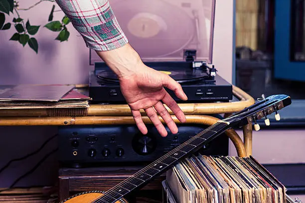 Photo of Man picking up guitar after listening to records