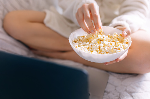 Woman resting on the bed and eating popcorn during watching film  on laptop at home