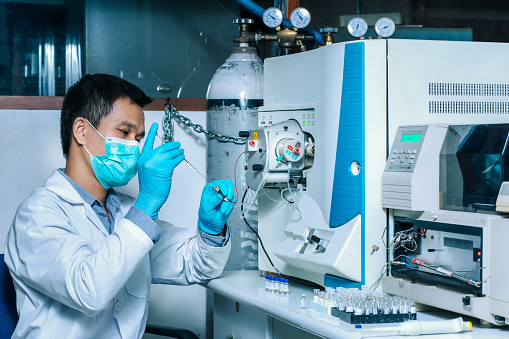 A scientist man injects a sample with a micro syringe into Mass Spectrometer to analyze samples, Mass spectrometry is used to measure mass per charge connected to Liquid Chromatography LC-MS