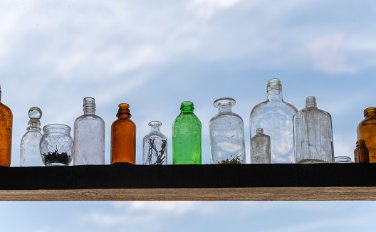 A variety of empty glass bottles arranged on a shelf against a blue sky.