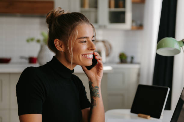 istock Confident young woman talking on mobile phone and smiling while working at home 1802410718