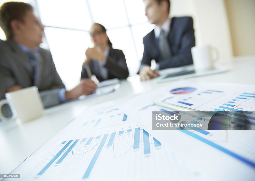 Business documents Close-up of business documents lying on the desk, office workers meeting in the background Data Stock Photo