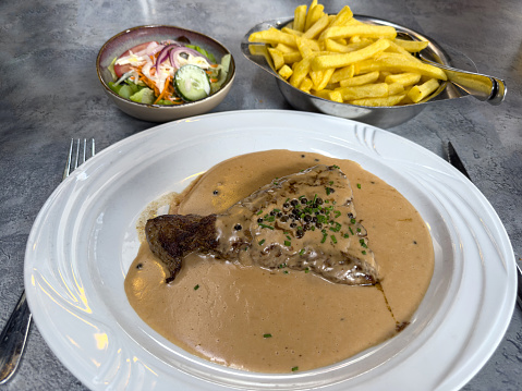 Grilled beef fillet steak with peppercorn sauce, served with French fries and a side salad