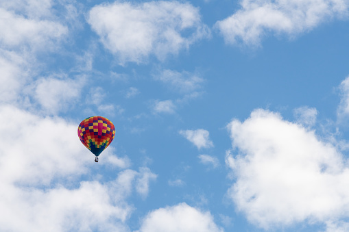 Colorful hot air balloon with people in a basket rises to the sky among the trees.