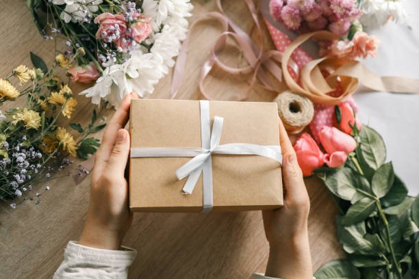 istock Gift box in hands with flowers at home 1802469439