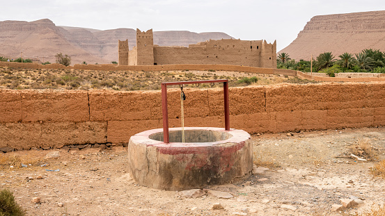 A water well with a traditional Moroccan fortress in the background, Atlas mountain gorge by Ziz river, Morocco