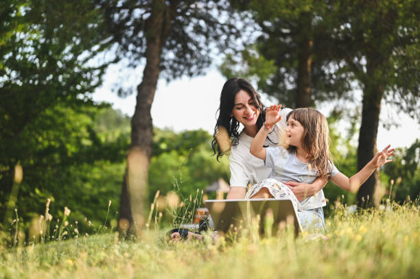 istock Cheerful family using computer in a parkland sitting on the grass. 1802491539