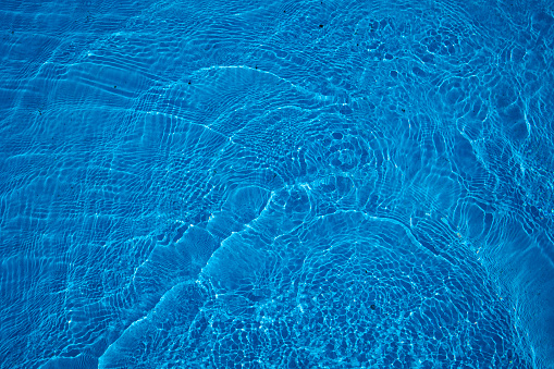 Reflecting water wave abstract surface on a sunny day and natural swirl texture, summer background. Water surface in vibrant blue. Abstract of water in swimming pool.
