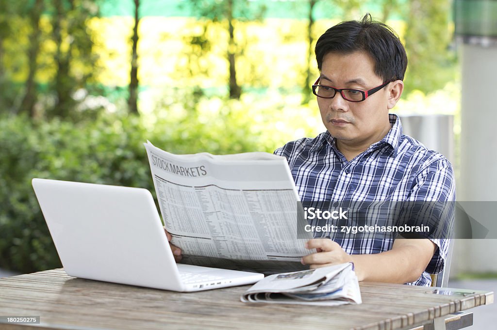 Азиатский мужчина, чтение финансовой газеты с белый ноутбук. - Стоковые фото Беспроводная технология роялти-фри