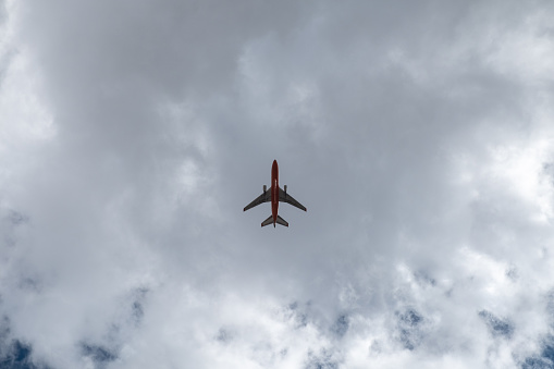 A passenger airplane flies directly overhead, outlined against a cloudy sky and lots of empty space.