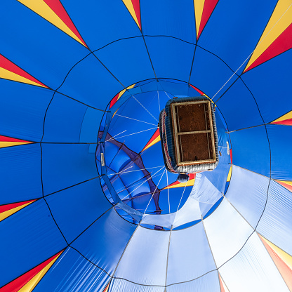 Looking up at a blue hot air balloon as it flies overhead, with a clear view into the envelope of the balloon, and of the pilot’s basket.