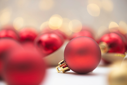 Close up of red and golden colored christmas baubles with christmas lights in the background.