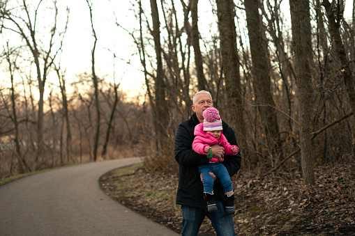 Grandpa does his best to hang on to a squirming 18 month old granddaughter while walking through the woods, Rochester, Minnesota  laughs