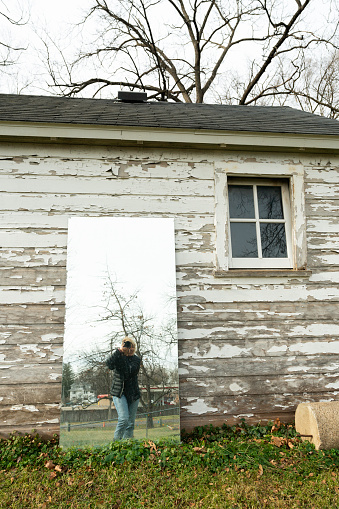 Reflection of woman in a mirror against a small old horse barn in town, Rochester, MN, USA