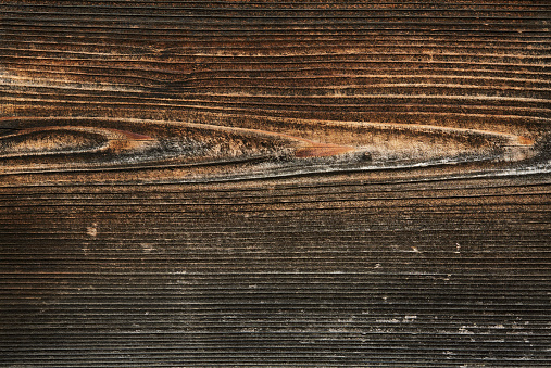 Weathered and scratched rustic wooden board.High angle view of a flat textured wooden board backgrounds. It has a beautiful nature and abstractive pattern. A close-up studio shooting shows details and lots of wood grain on the wood table. The piece of wood at the surface of the table also appears rich wooden material on it. The wood is dark brown color with darker brown lines and pattern on the bottom. Flat lay style. Its high-resolution textured quality.The close-up gives a direct view on the table, showing cracks and knotholes in the wood.