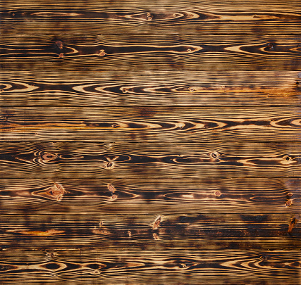 Weathered and scratched rustic wooden board.High angle view of a flat textured wooden board backgrounds. It has a beautiful nature and abstractive pattern. A close-up studio shooting shows details and lots of wood grain on the wood table. The piece of wood at the surface of the table also appears rich wooden material on it. The wood is dark brown color with darker brown lines and pattern on the bottom. Flat lay style. Its high-resolution textured quality.The close-up gives a direct view on the table, showing cracks and knotholes in the wood.