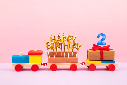 Wooden colorful toy train with Happy Birthday candles and number 2, on pink background