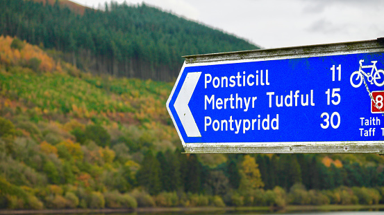 Autumn colours on the mountains of the Brecon Beacons. The blue and white road sign points to the direction for Ponsticill Reservoir, Merthyr Tydfil and Pontypridd and the Taff Trail cycle route