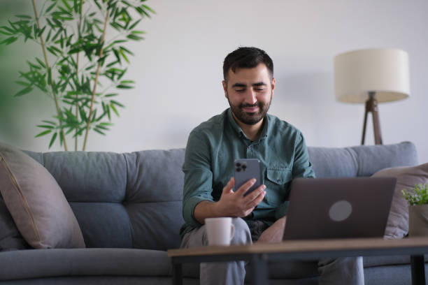 istock young man making a video call via phone while sitting on the couch 1802552823