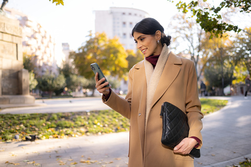 Confident and emancipated businesswoman walking in a big city, portrait lady with a cell phone, texting messages in working chat, reading financial news