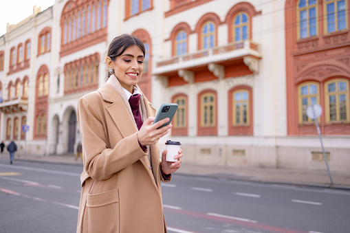 Businesswoman using a mobile phone - a trendy business working woman in the city streets looking at a smartphone
