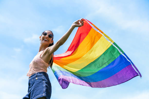 istock Joyful Woman Celebrating Pride with Rainbow Flag Under Sunny Sky 1802574138