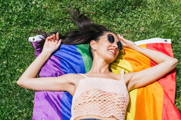 istock Smiling Woman Relaxing on Rainbow Pride Flag in Sunny Park 1802575248
