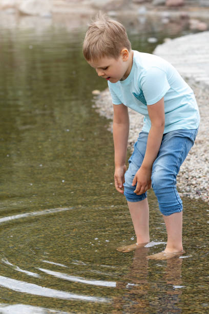 istock A small cautious boy in blue clothes wades into the water and tries to pull up his pants so they don't get wet 1802575792