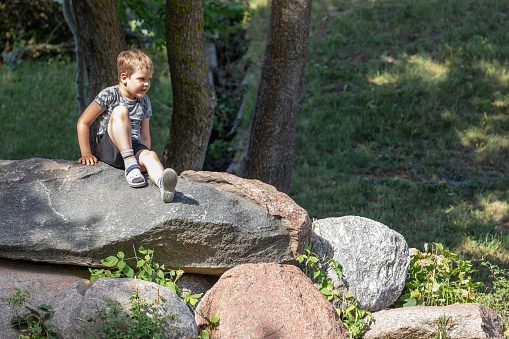 Portrait of a small boy sitting on top of large rocks.