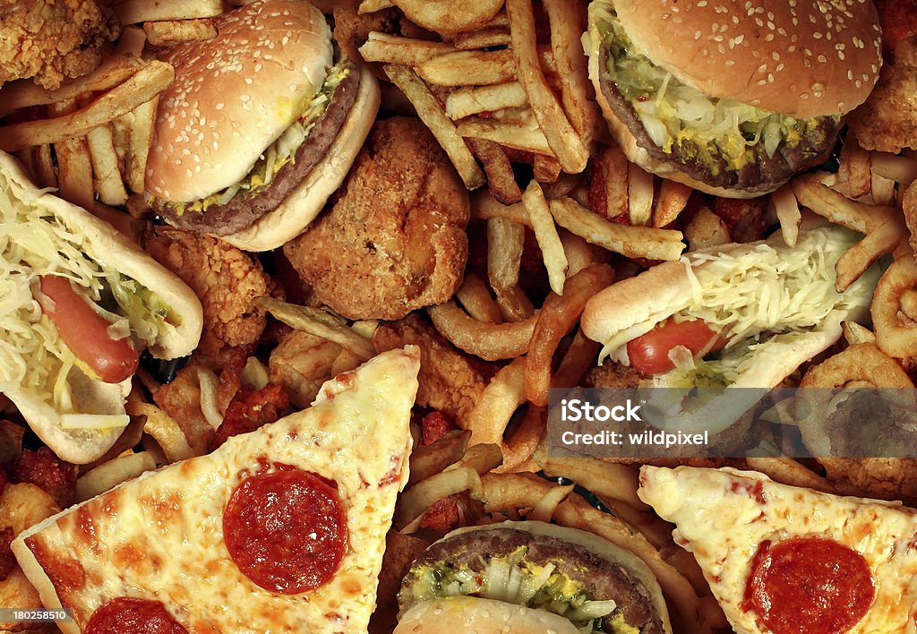 Fast food items like hot dogs, hamburgers, fries and pizza Fast food concept with greasy fried restaurant take out as onion rings burger and hot dogs with fried chicken french fries and pizza as a symbol of diet temptation resulting in unhealthy nutrition. Unhealthy Eating Stock Photo