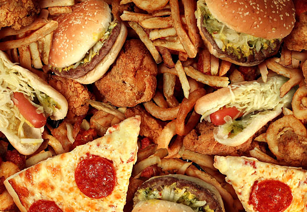 Fast food items like hot dogs, hamburgers, fries and pizza Fast food concept with greasy fried restaurant take out as onion rings burger and hot dogs with fried chicken french fries and pizza as a symbol of diet temptation resulting in unhealthy nutrition. unhealthy eating stock pictures, royalty-free photos & images