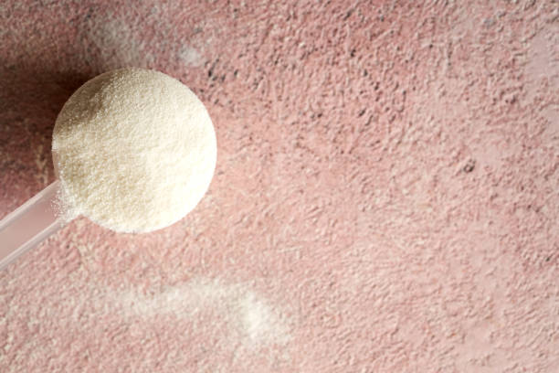 Collagen powder in a plastic measuring cup on pink background with copy space