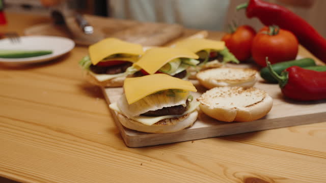 A Woman Places Slices of Cheese on the Burgers. Homemade Food. Ingredients Are Spread Out on the Table.