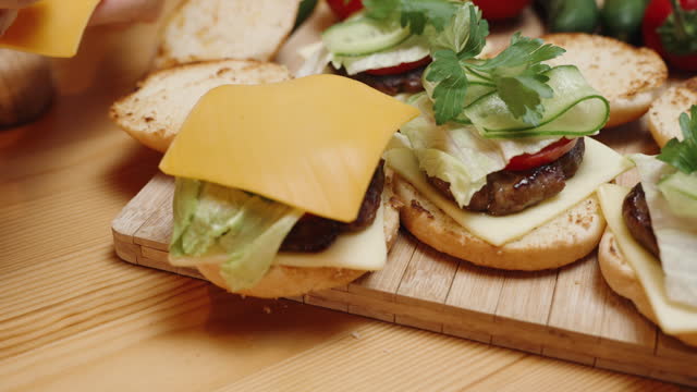 The Preparation of Burgers in a Homey Setting, slices of cheese are placed on top. Ingredients are on the table, and the burgers are almost ready. In slow motion.