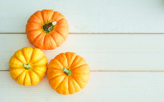 Various fresh ripe pumpkins on a white wooden background