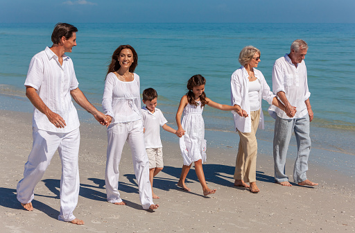 Happy family of grandfather, grandmother, mother, father and two children, son and daughter, walking holding hands on a deserted sunny beach