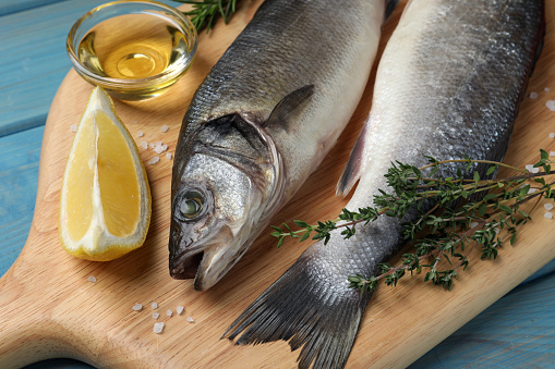 Sea bass fish and ingredients on light blue wooden table, closeup