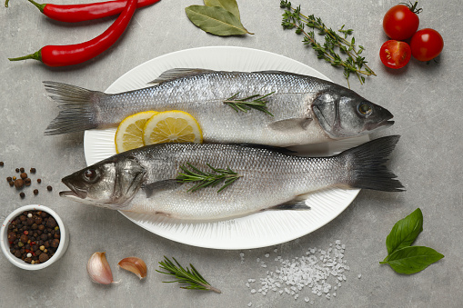 Sea bass fish and ingredients on grey table, flat lay