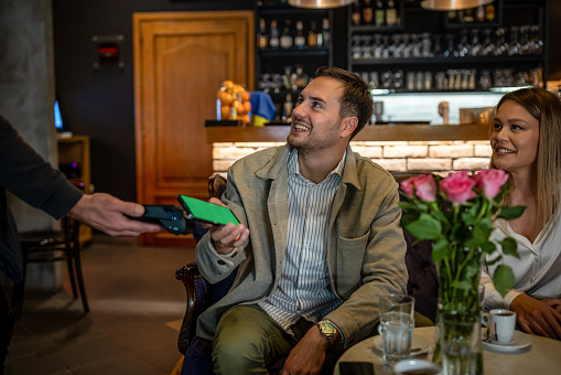 Man and woman making a contactless payment to the waitress at a cafe using his cell phone