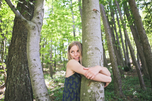 Blonde girl hugging a tree trunk in a forest