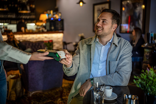 Photo of young man paying with contactless credit card at cafe