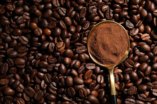 Spoon with ground coffee on roasted beans, top view. Space for text