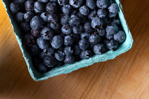 A carton of blueberries on a wooden cutting board.